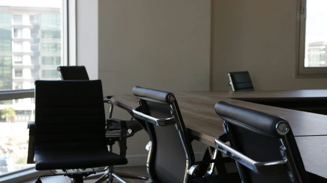 a row of empty black office chairs in front of a long desk