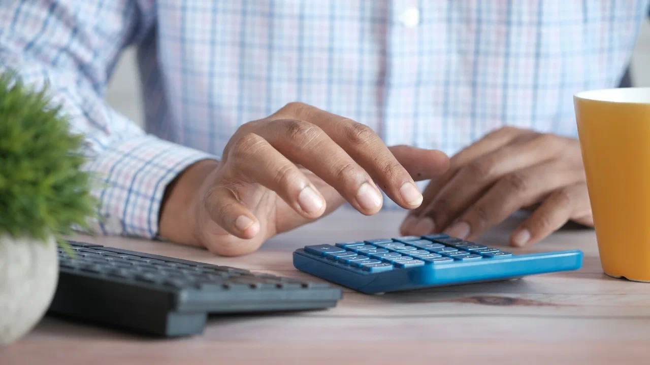a hand working a desk calculator next to a coffee mug