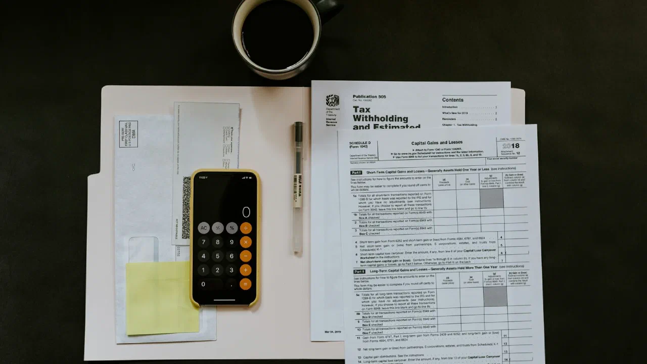 a printed tax form on a white folder beside a ballpoint pen and a smartphone