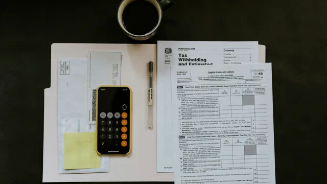 a printed tax form on a white folder beside a ballpoint pen and a smartphone
