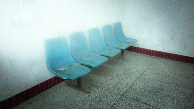 a row of empty blue plastic chairs in a waiting room